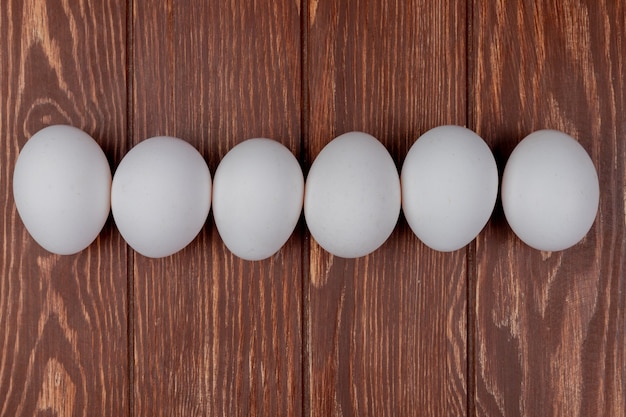 Vista superior de huevos de gallina blanca fresca dispuesta en línea sobre un fondo de madera