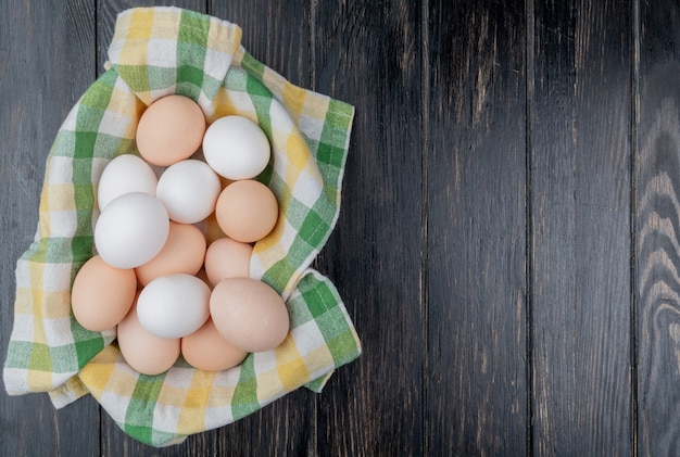 Vista superior de huevos de gallina fresca sobre mantel facturado sobre un fondo de madera con espacio de copia