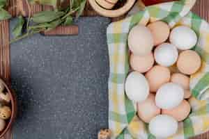 Foto gratuita vista superior de huevos de gallina sobre un mantel marcado con huevos de codorniz en un tazón de madera con hojas sobre un fondo de madera con espacio de copia