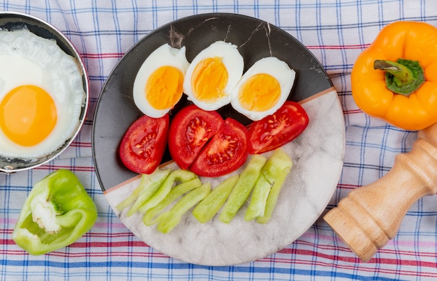 Vista superior de huevos hervidos a la mitad en un plato con rodajas picadas de tomates y pimientos verdes sobre un fondo de mantel marcado