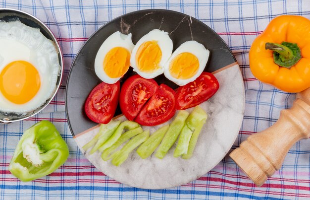 Vista superior de huevos hervidos a la mitad en un plato con rodajas picadas de tomates y pimientos verdes sobre un fondo de mantel marcado