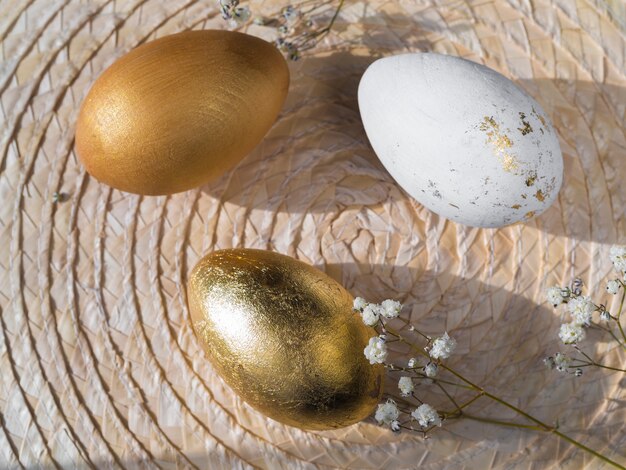 Vista superior de huevos de pascua de color dorado sobre mantel individual con gypsophila