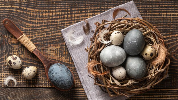 Vista superior de los huevos de pascua en el nido de ramitas con cuchara de madera y plumas