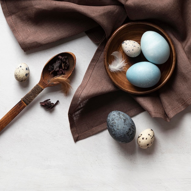 Vista superior de huevos de pascua en plato con cuchara de madera y plumas