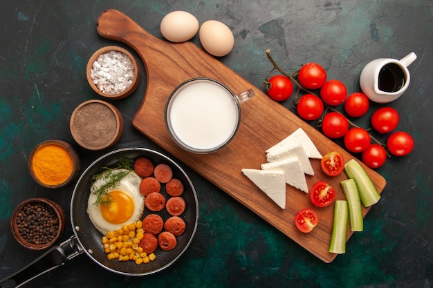 Foto gratuita vista superior de huevos revueltos con salchichas y con condimentos de tomates frescos sobre fondo oscuro