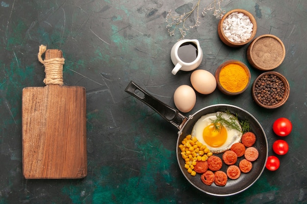 Foto gratuita vista superior de huevos revueltos con salchichas y diferentes condimentos en el fondo verde oscuro