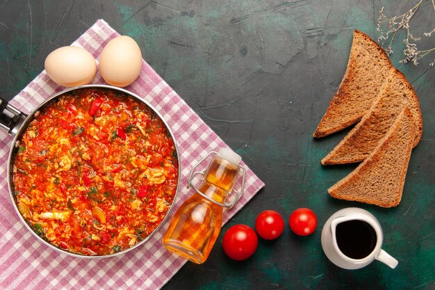 Vista superior de huevos revueltos con tomates y hogazas de pan sobre el fondo verde oscuro