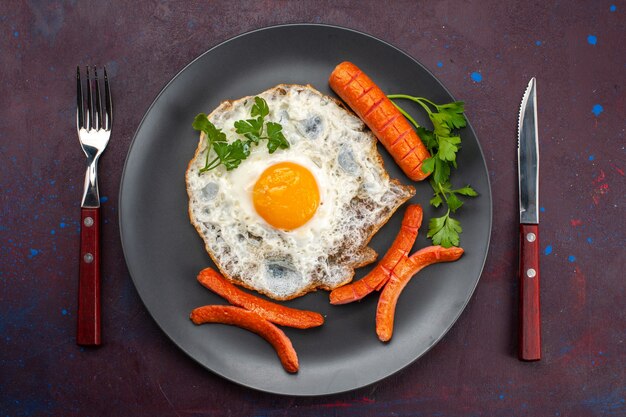 Vista superior de huevos revueltos con verduras y salchichas dentro de la placa sobre la superficie oscura