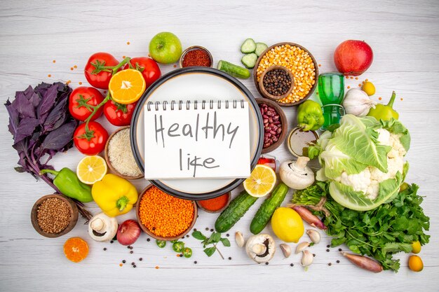 Vista superior de una inscripción de vida sana en un cuaderno de espiral en una olla blanca en la colección de verduras frescas para la cena vegetariana que cocina en el fondo blanco