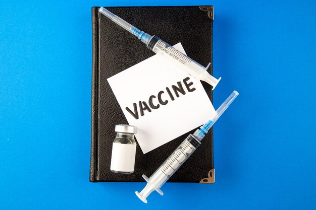 Vista superior de inyecciones de antivirus con copybook y vacuna en la superficie azul de la medicina del virus de la medicina hospitalaria covid- lab cura la salud