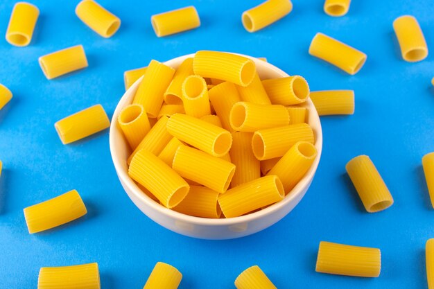 Una vista superior italia pasta seca formada poca pasta cruda amarilla dentro de un recipiente redondo de color crema aislado en el fondo azul pasta de comida italiana de espagueti