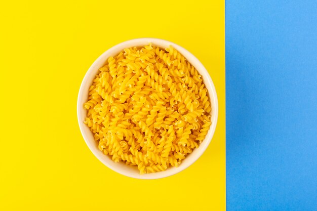 Una vista superior italiana pasta seca formada poco amarillo pasta cruda dentro de un recipiente redondo de color crema aislado en el azul-amarillo