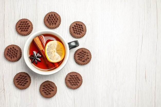 Vista superior izquierda té limón canela redondeado con galletas en la mesa de madera blanca