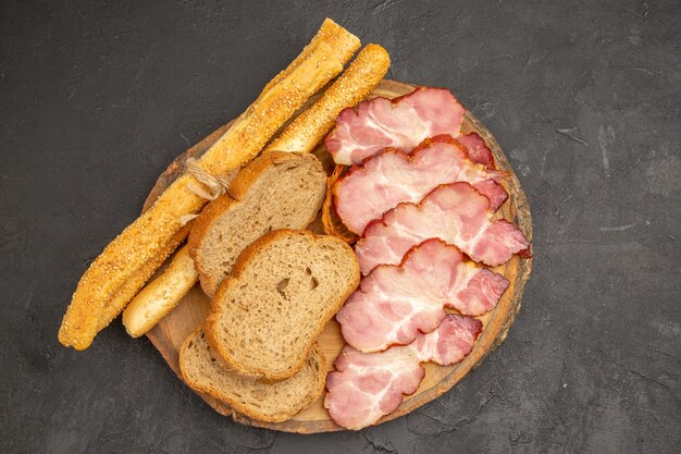 Vista superior de jamón fresco en rodajas con bollos y rebanadas de pan sobre fondo oscuro