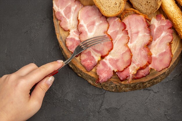 Vista superior de jamón fresco en rodajas con rebanadas de pan sobre fondo oscuro