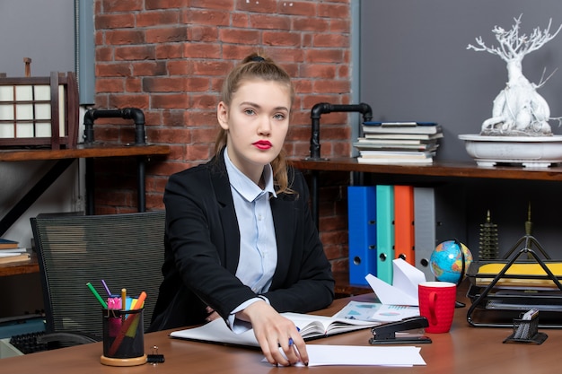 Vista superior de la joven asistente femenina segura sentada en su escritorio en la oficina