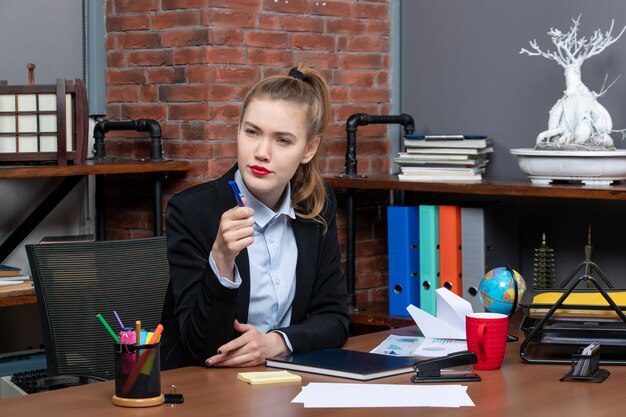 Vista superior de la joven asistente femenina segura sentada en su escritorio en la oficina