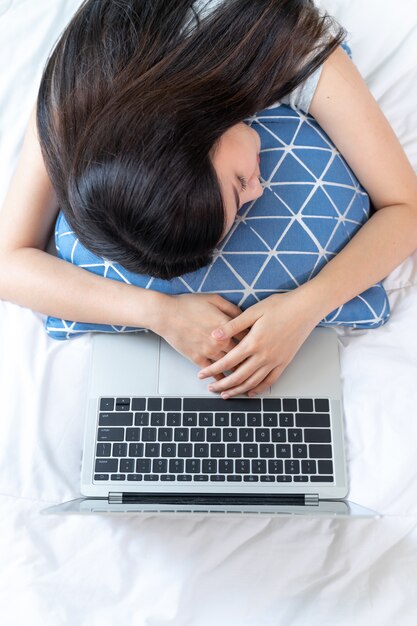 Vista superior joven y bella mujer se quedó dormida en la cama después de la fatiga de trabajar con la computadora portátil