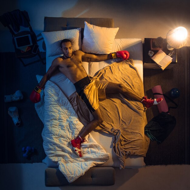 Vista superior del joven boxeador profesional, luchador durmiendo en su habitación en ropa deportiva con guantes