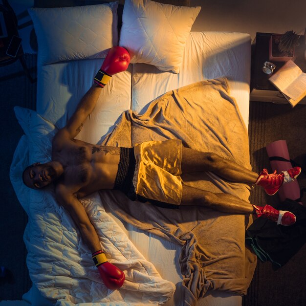 Vista superior del joven boxeador profesional, luchador durmiendo en su habitación en ropa deportiva con guantes