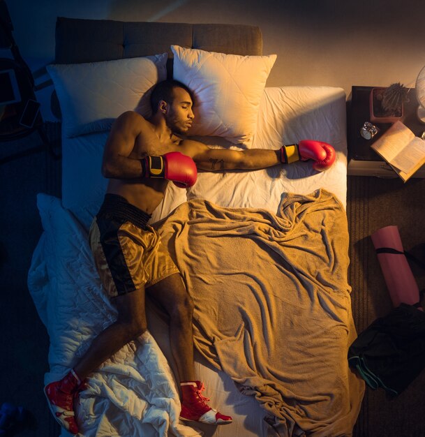 Vista superior del joven boxeador profesional, luchador durmiendo en su habitación en ropa deportiva con guantes