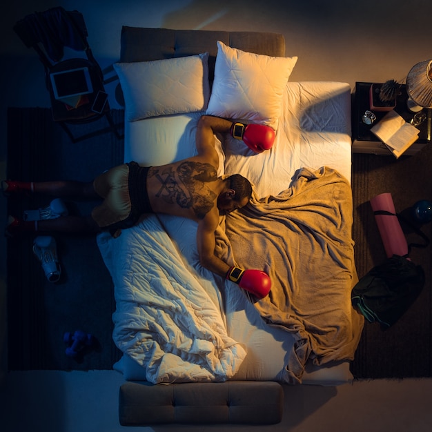 Vista superior del joven boxeador profesional, luchador durmiendo en su habitación en ropa deportiva con guantes