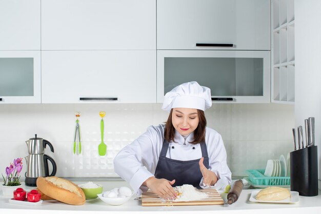 Vista superior de la joven chef femenina concentrada en uniforme de pie detrás de la mesa cocinando comida en la cocina blanca