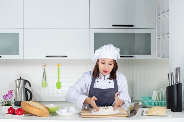 Vista superior de la joven chef ocupada en uniforme de pie detrás de la mesa cocinando comida en la cocina blanca