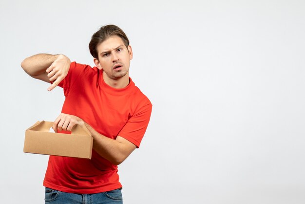 Vista superior del joven confundido y emocional en blusa roja con caja sobre fondo blanco.