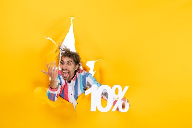 Vista superior del joven enojado y emocional que muestra el diez por ciento en un agujero rasgado en papel amarillo