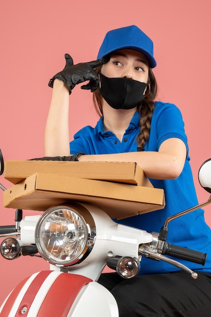 Vista superior del joven mensajero con máscara médica y guantes sosteniendo cajas pensando profundamente en melocotón pastel