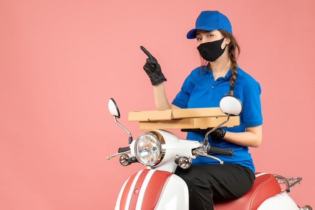 Foto gratuita vista superior del joven mensajero mujer curiosa con máscara médica y guantes sentado en scooter entregando pedidos en melocotón pastel