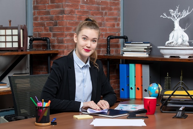 Vista superior de la joven oficinista sentada en su escritorio y doblando la página
