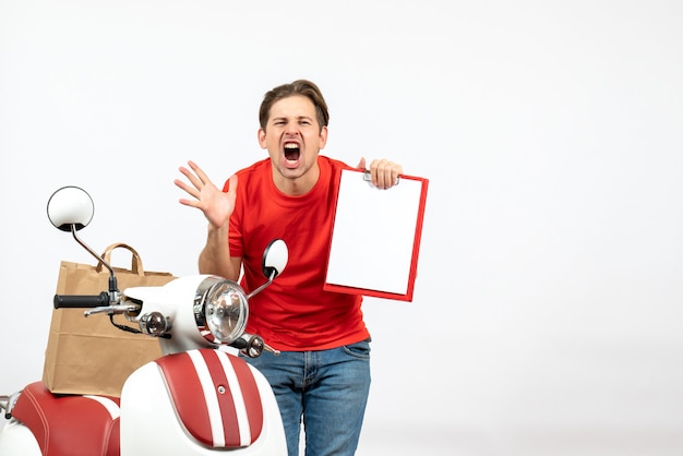 Foto gratuita vista superior del joven repartidor nervioso en uniforme rojo de pie cerca de scooter mostrando documento haciendo gesto de anteojos gritando en la pared blanca