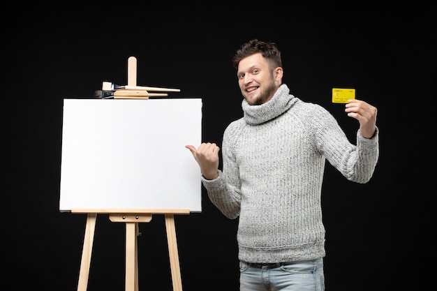 Vista superior del joven y sonriente artista barbudo con tarjeta bancaria en negro aislado