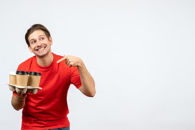 Vista superior del joven sonriente en blusa roja señalando órdenes en la pared blanca