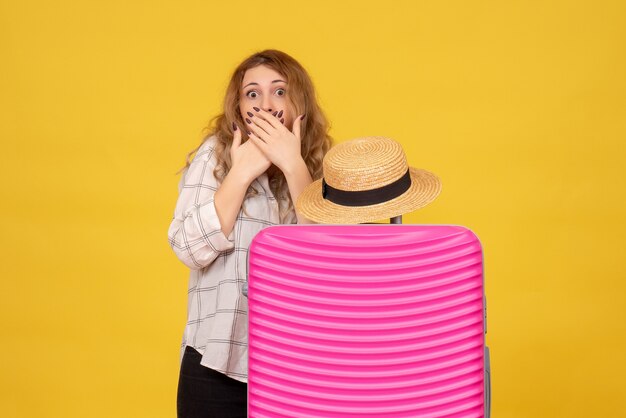 Vista superior de la joven sorprendida de pie detrás de su bolso rosa