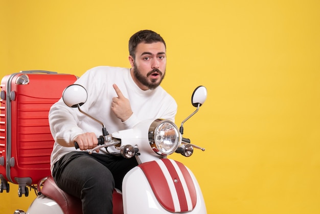 Vista superior del joven sorprendido sentado en la motocicleta con la maleta y apuntando hacia arriba en amarillo