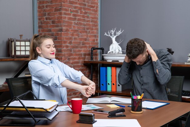 Vista superior del joven y su compañera de trabajo sentados en la mesa sintiéndose cansados en el ambiente de oficina
