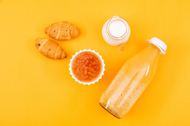 Vista superior de jugo con cruasanes y mermelada, leche en superficie amarilla horizontal