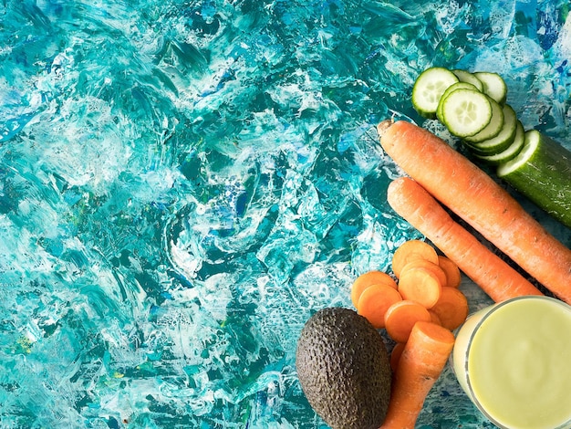 Vista superior de jugo de desintoxicación junto a zanahorias, pepino y aguacate sobre fondo de madera de colores