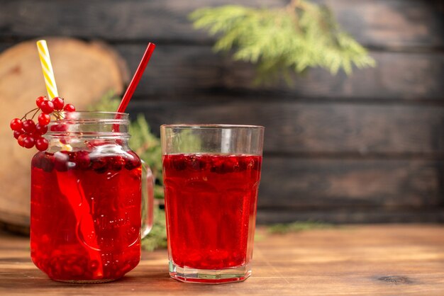 Vista superior de jugo de grosella fresca orgánica natural en una botella servida con tubos y en un vaso en el lado derecho sobre una mesa de madera