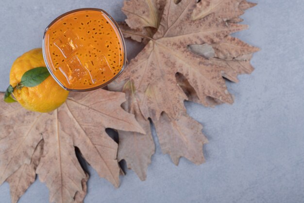 Vista superior del jugo de mandarina con mandarina fresca en hojas secas sobre fundamento gris