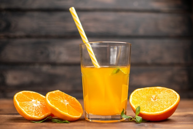 Vista superior de jugo de naranja fresco en un vaso servido con un tubo de menta y limas de naranja sobre una mesa de madera