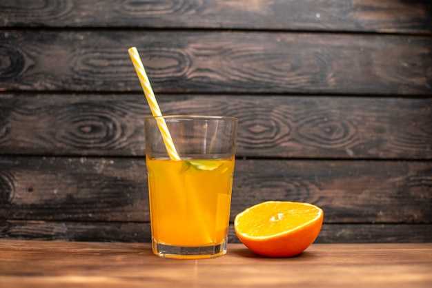 Vista superior de jugo de naranja fresco en un vaso servido con un tubo de menta y limón naranja sobre una mesa de madera