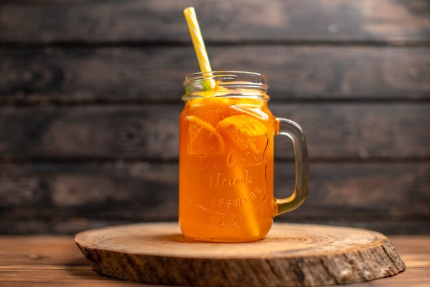 Vista superior de jugo de naranja fresco en un vaso con tubo en una bandeja de madera sobre fondo marrón