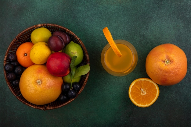 Vista superior de jugo de naranja en un vaso con pomelo lima limón melocotón cereza ciruela naranja y ciruela en una canasta sobre un fondo verde
