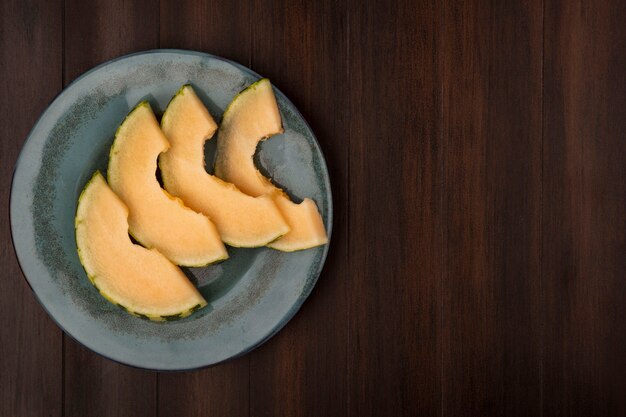 Vista superior de jugosas rodajas de melón cantalupo en un plato sobre una pared de madera con espacio de copia