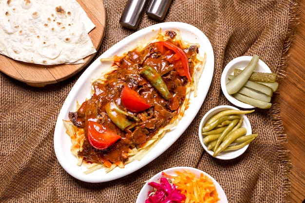Vista superior de kebab de carne turca con salsa de tomate picante servido con pepinillos