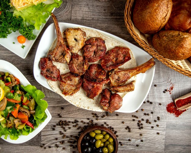 Vista superior de kebab de costillas de cordero con ensalada de verduras y granos de pimienta en una mesa de madera